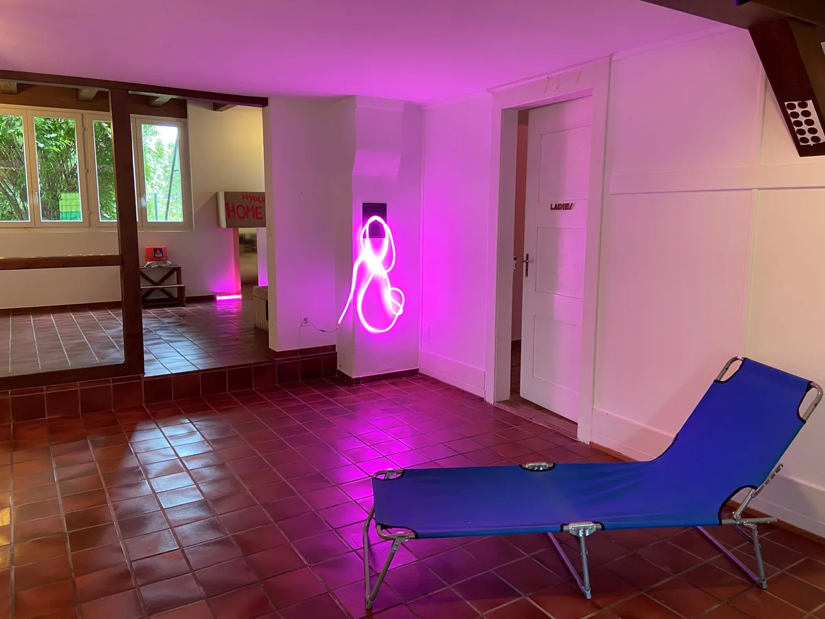 Ein blauer Liegestuhl und dahinter eine pinke Lichterkette an einer Wand.